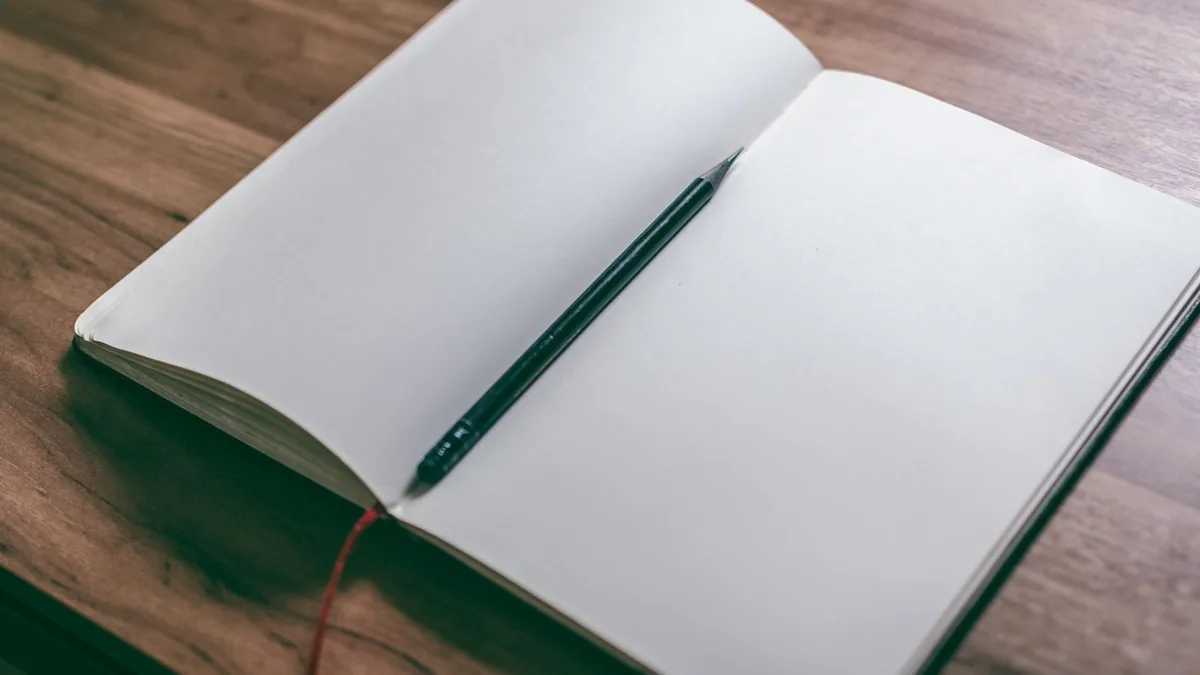 木の机の上で開いた白紙のノートと黒い鉛筆